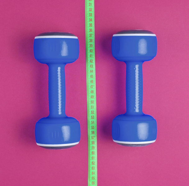 Das Konzept des Abnehmens. Blaue Kunststoffhanteln, Lineal auf rotem Hintergrund. Sport, Fitness. Ansicht von oben. Flache Lage - Foto, Bild