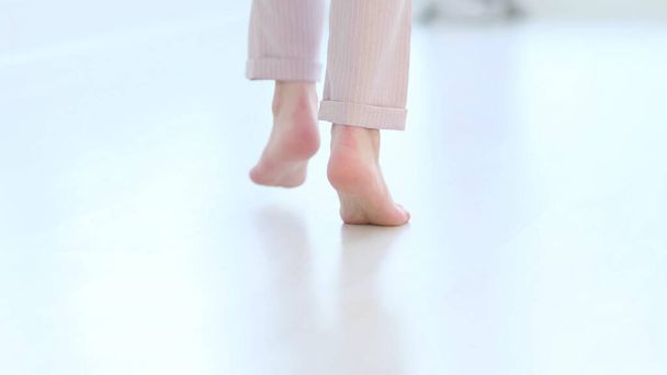 Side close up view of unrecognizable woman feet legs, barefoot girl standing indoors inside of modern home enjoy warm wooden heated floor. soft focus - 写真・画像