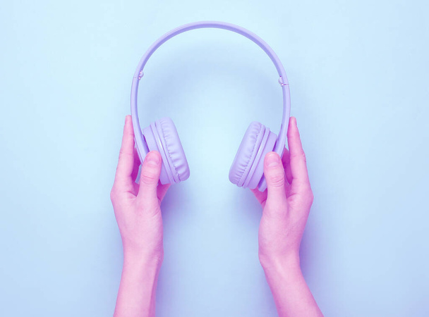 女性の手は青いパステルの背景に無線耳のヘッドフォンを保持しています。デュオトン効果。ミニマリズム。トップ表示 - 写真・画像