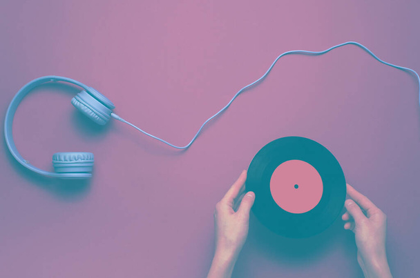 Les mains des femmes détiennent un disque vinyle sur fond violet avec un casque au-dessus de l'oreille. Pop culture, style rétro, années 80. Minimalisme. Vue de dessus. Pose plate - Photo, image