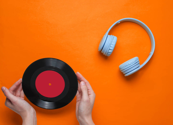 Frauenhände halten Schallplatten auf orangefarbenem Hintergrund mit Ohr-Kopfhörer. Popkultur, Retro-Stil, 80er Jahre. Minimalismus. Ansicht von oben. Flache Lage - Foto, Bild