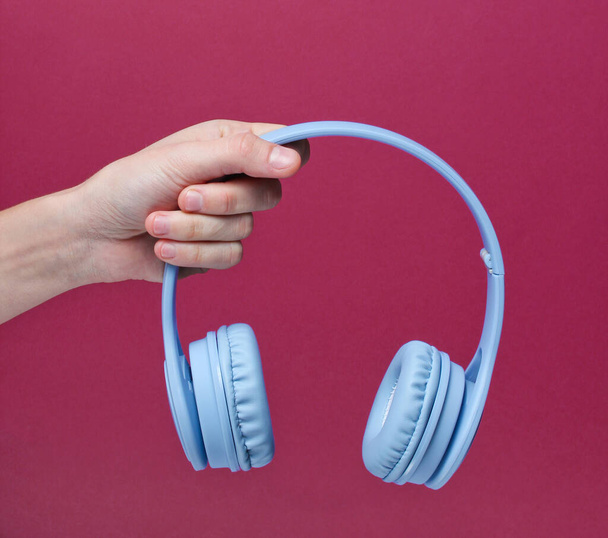 Mão feminina segurando modernos fones de ouvido azuis sem fio no fundo vermelho. - Foto, Imagem