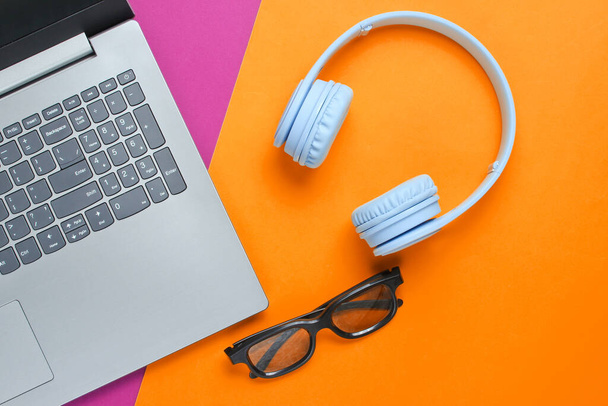 Modern gadgets. Laptop, wireless headphones, 3D glasses on a purple-yellow background. - Photo, image