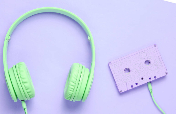紫色の背景にオーディオカセット付きのヘッドフォン。レトロなスタイルでミニマリズム。平置きだ。トップ表示. - 写真・画像