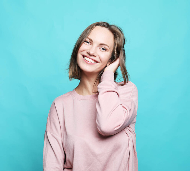 Young cute smiling blond female wear pink sweater over blue background. Lifestyle, emotion and people concept. - Foto, Bild