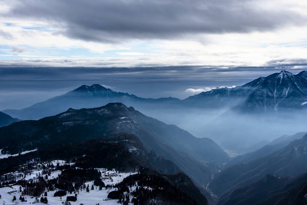Karlı tepeleri ve sisli vadileri olan dağlık dağ tepeleri ve Tonezza, Vicenza, İtalya 'da mavi katmanlı dağ manzaraları. - Fotoğraf, Görsel