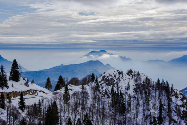 alpine landscape with snowy peaks and misty valleys, with menacing sky snow mountain peaks and blue layering in Tonezza, Vicenza, Italy - Photo, Image