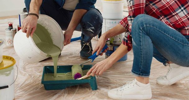 Close up of Caucasian happy nice married couple man and woman pouring paint and preparing for painting house. Wife helping her husband to repair home room working together. Renovation and improvement - 写真・画像