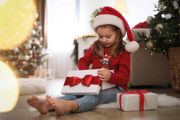 Cute little girl opening gift box in room decorated for Christmas - Фото, изображение