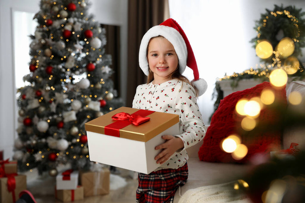 Cute little girl holding gift box in room decorated for Christmas - Fotoğraf, Görsel
