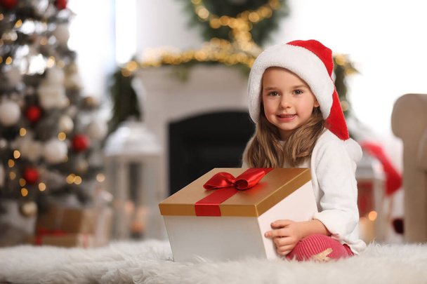 Cute little girl holding gift box in room decorated for Christmas - Fotografie, Obrázek