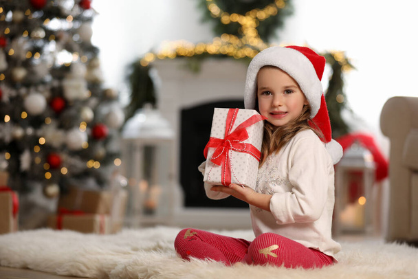 Cute little girl holding gift box in room decorated for Christmas - 写真・画像
