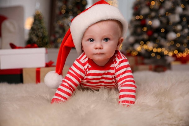 Lindo bebé en pijama brillante y sombrero de Santa en el suelo en casa. Traje de Navidad - Foto, imagen