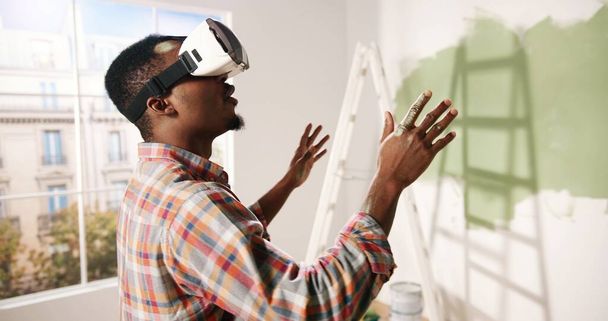 Close up of African American young impressed excited man stands in room wearing VR glasses and looking at new redesigned renewed apartment using modern innovations. Virtual reality technology - 写真・画像