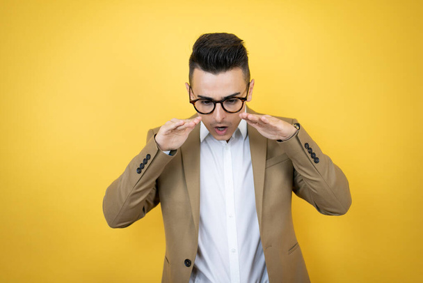 Young business man over isolated yellow background shouting and screaming loud down with hands on mouth - Valokuva, kuva