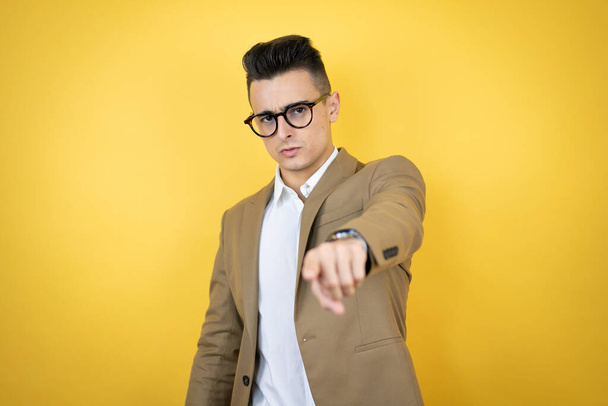 Young business man over isolated yellow background serious pointing to the front with finger - Photo, Image