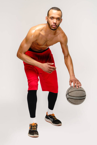 Muscular african american sportsman playing basketball shitless over light grey background - 写真・画像
