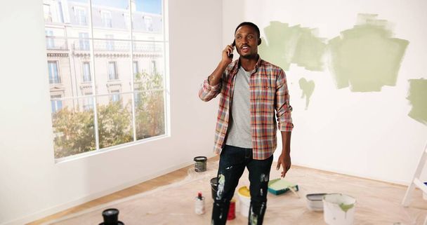 Close up of joyful African American handsome guy smiling and speaking on cellphone in apartment in good mood. Happy man calling on smartphone about home repair. Renovation concept - Φωτογραφία, εικόνα