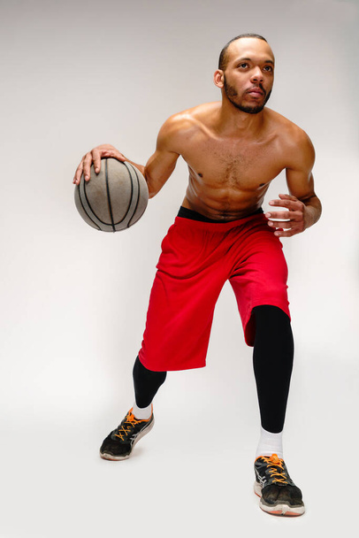 Muscular african american sportsman playing basketball shitless over light grey background - Foto, afbeelding