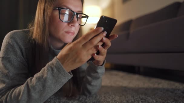 Nő szemüveges fekszik a padlón, és használja okostelefon este - Felvétel, videó