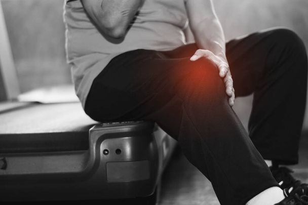 opieka zdrowotna i koncepcja problemu - nieszczęśliwy starszy mężczyzna cierpiący na ból kolana siedzi na bieżni, czarno-białe tło - Zdjęcie, obraz