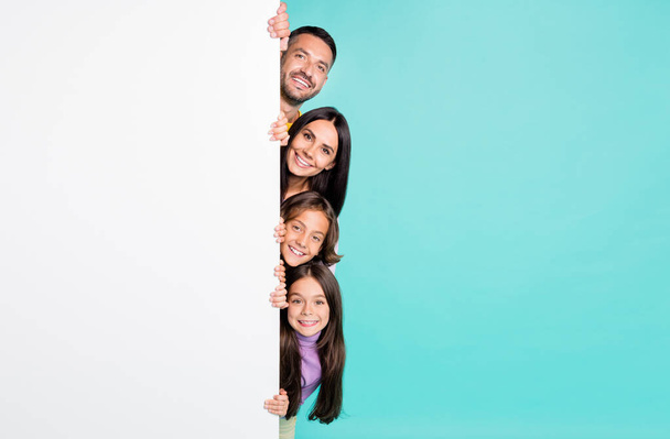Photo portrait of full family with small children peaking from the side of white banner poster isolated on vivid turquoise colored background - Photo, Image