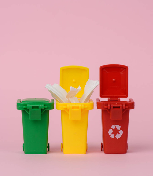 τρία πολύχρωμα πλαστικά δοχεία σε ροζ φόντο, η έννοια της ορθής διαλογής των απορριμμάτων για περαιτέρω ανακύκλωση - Φωτογραφία, εικόνα
