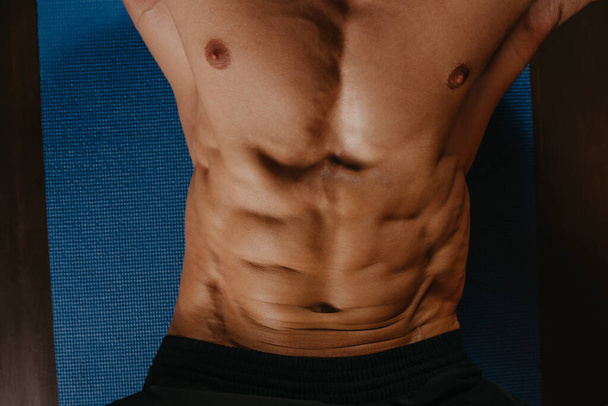 A photo from above of the abs of a bodybuilder during doing crunches on a blue yoga mat. - Photo, Image