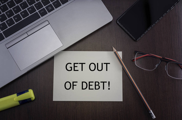 Get out of debt card. Top view of office table desktop background with laptop, phone, glasses and pencil with card with inscription get out of debt. Business concept. - Photo, Image