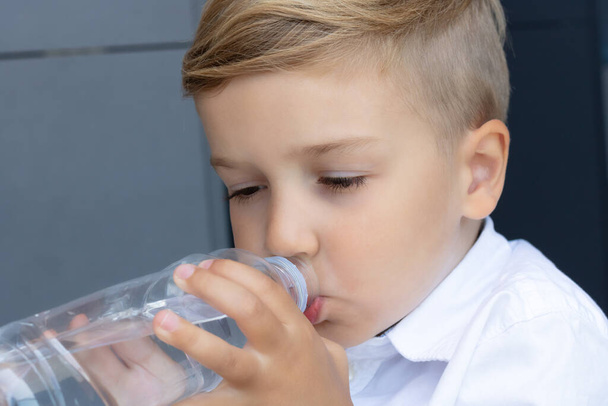 Милый маленький мальчик пьет воду из пластиковой бутылки.  - Фото, изображение