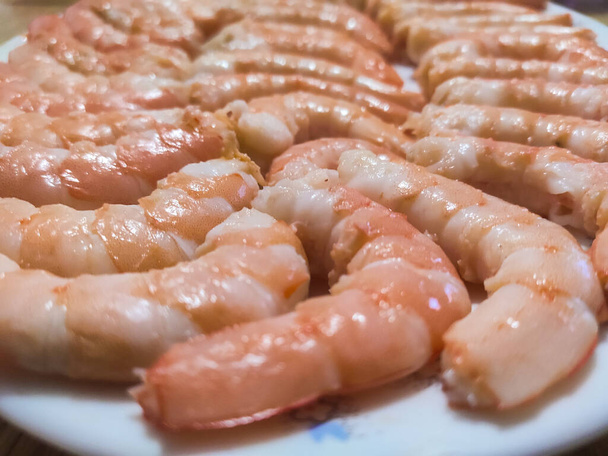 Crevettes entières cuites et pelées placées ensemble sur une assiette blanche. Fruits de mer typiques pour les déjeuners et dîners de Noël. Photographie horizontale. - Photo, image