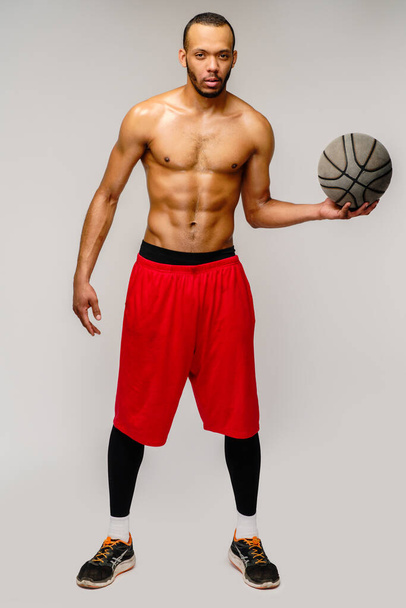 Muscular african american sportsman playing basketball shitless over light grey background - Photo, image