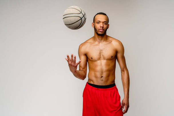 Muscular african american sportsman playing basketball shitless over light grey background - Foto, immagini