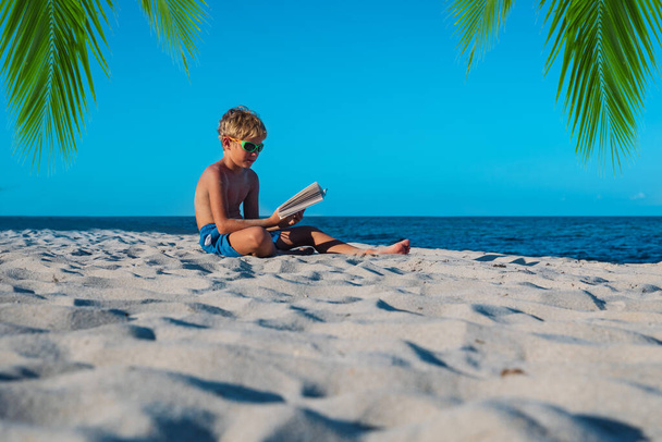 fiú olvasás könyv homokos tengerparton, gyerek tanulás nyaralás - Fotó, kép