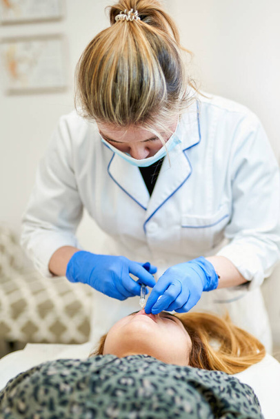 De arts cosmetoloog maakt Lip augmentatie procedure van een mooie vrouw in een schoonheidssalon - Foto, afbeelding