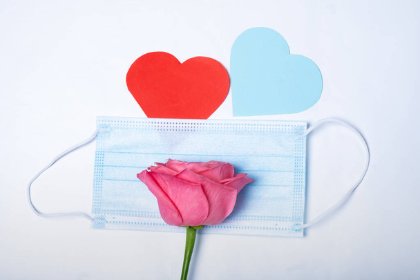 Two hearts covered with a medical mask and a rose. Valentine's day and coronavirus concept. - Photo, Image