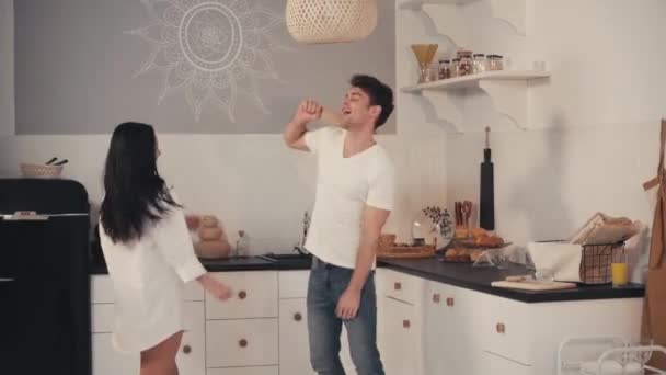 wesoły mężczyzna trzyma wałek podczas tańca z dziewczyną w kuchni - Materiał filmowy, wideo