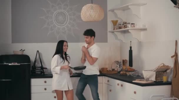 Nuori pari hauskaa tanssiessaan valssaustappi ja paistinpannu keittiössä - Materiaali, video