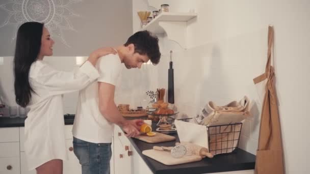 aistillinen nainen viettelee poikaystävä leikkaamalla tuoretta oranssi keittiössä - Materiaali, video