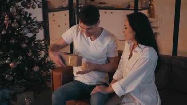 Junger Mann beschenkt verblüffte Freundin in der Nähe des Weihnachtsbaums - Filmmaterial, Video