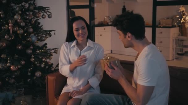 Nuori nainen esittää lahja hämmästynyt mies lähellä joulukuusi - Materiaali, video