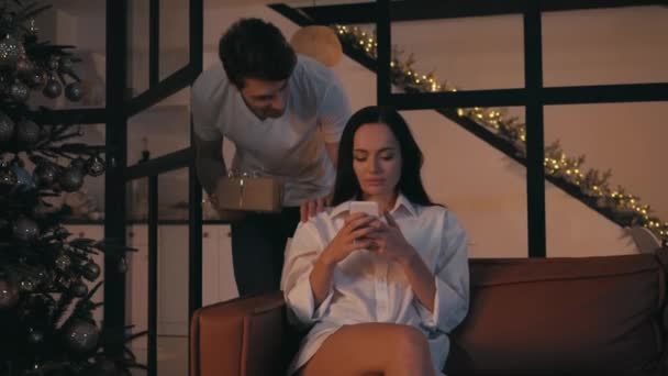 νεαρός άνδρας παρουσιάζει χριστουγεννιάτικο δώρο στην ευτυχισμένη γυναίκα κουβεντιάζοντας στο smartphone - Πλάνα, βίντεο