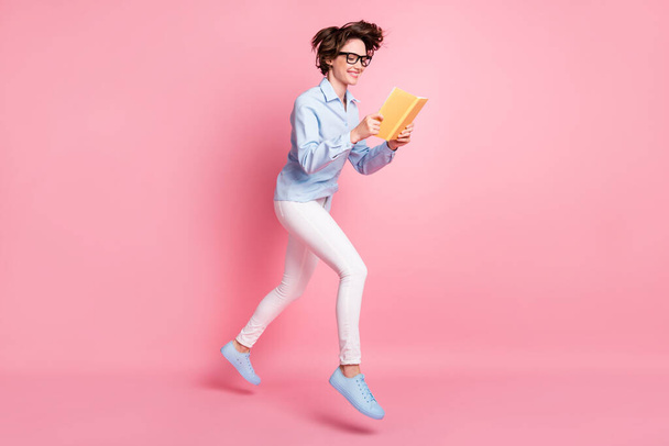 Full length body size profile side view of her she nice attractive skinny cheerful cheery brown-haired girl jumping reading diary walking free time isolated pink pastel color background - Foto, Imagem