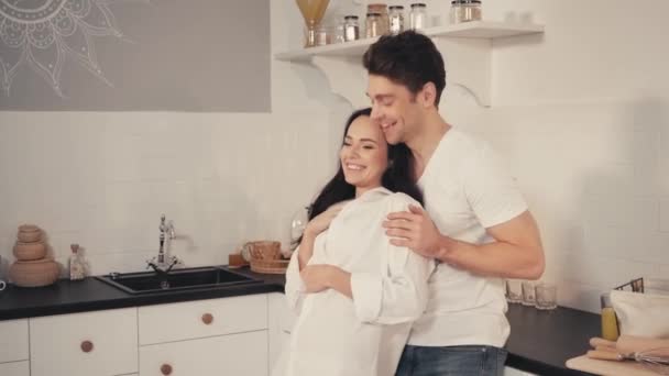 uomo ridente abbracciando fidanzata e puntando con il dito in cucina - Filmati, video