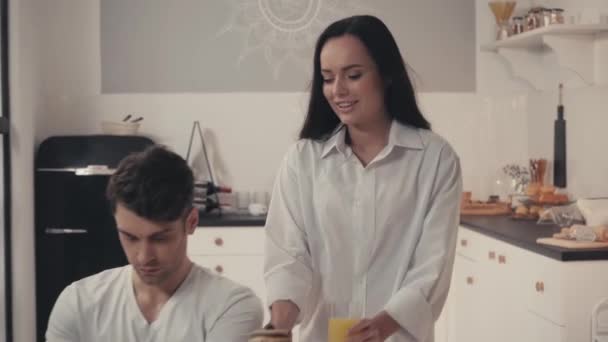sexy žena servírující snídani v blízkosti volné noze pracující na notebooku v kuchyni - Záběry, video