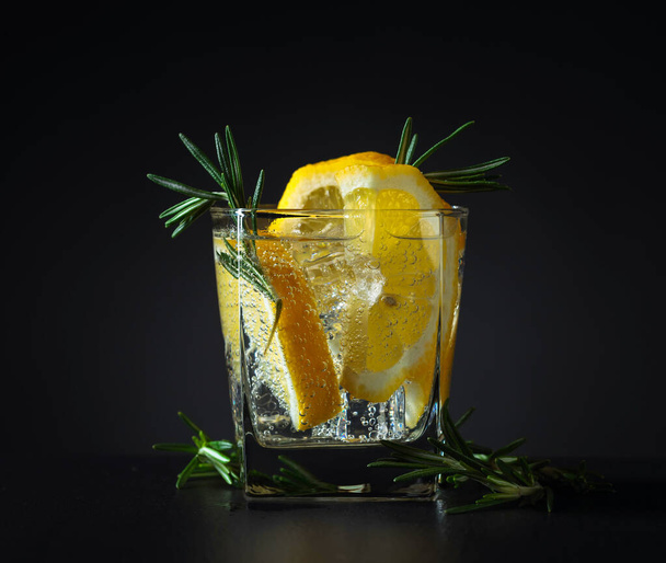 Cocktail Gin Tonic mit Zitrone und Rosmarin auf schwarzem Hintergrund. - Foto, Bild