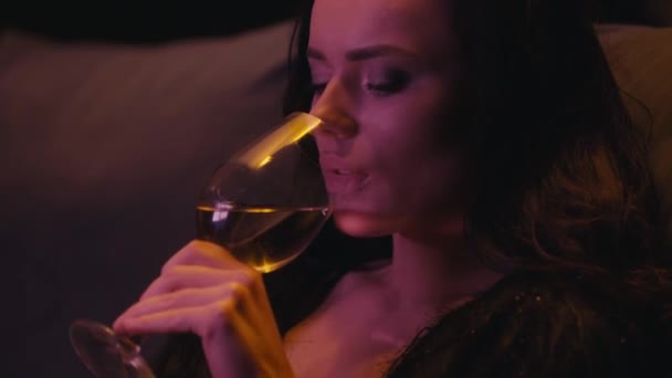 joven morena bebiendo vino blanco sobre fondo oscuro - Metraje, vídeo