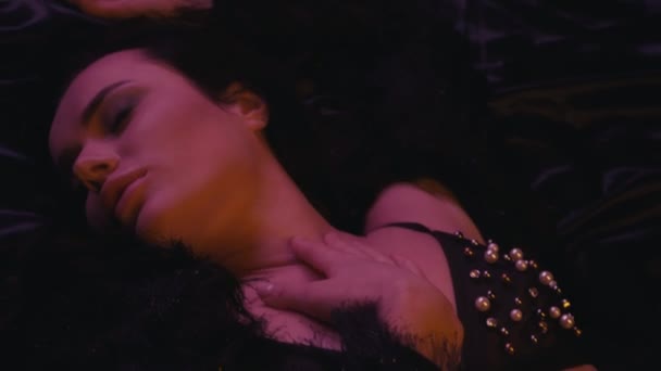 sexy młoda kobieta w biustonosz leżąc i dotykając się na ciemnym tle  - Materiał filmowy, wideo