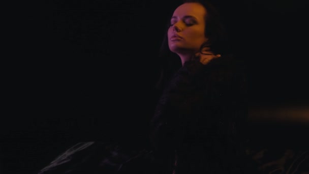 sexy kobieta w biustonosz i faux futro płaszcz dotykając się na ciemnym tle  - Materiał filmowy, wideo