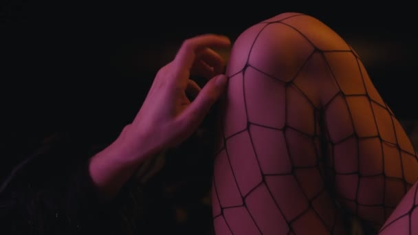 donna seducente toccare le gambe in calze a rete su sfondo scuro  - Filmati, video